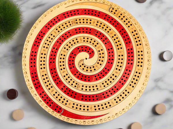 Round wooden cribbage board with red and beige spiral design on a gray background