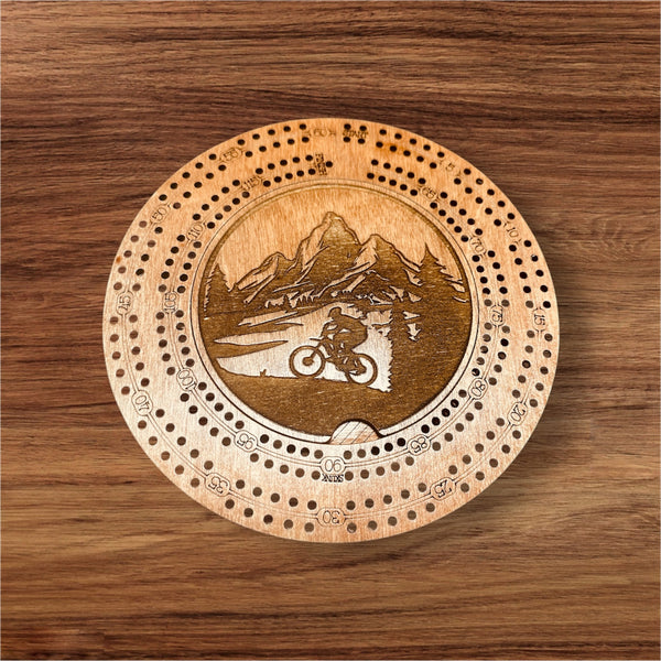 Wooden cribbage board with mountain and bike design on a wooden surface