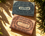 Two wooden cribbage boards on a wooden surface with plants in the background