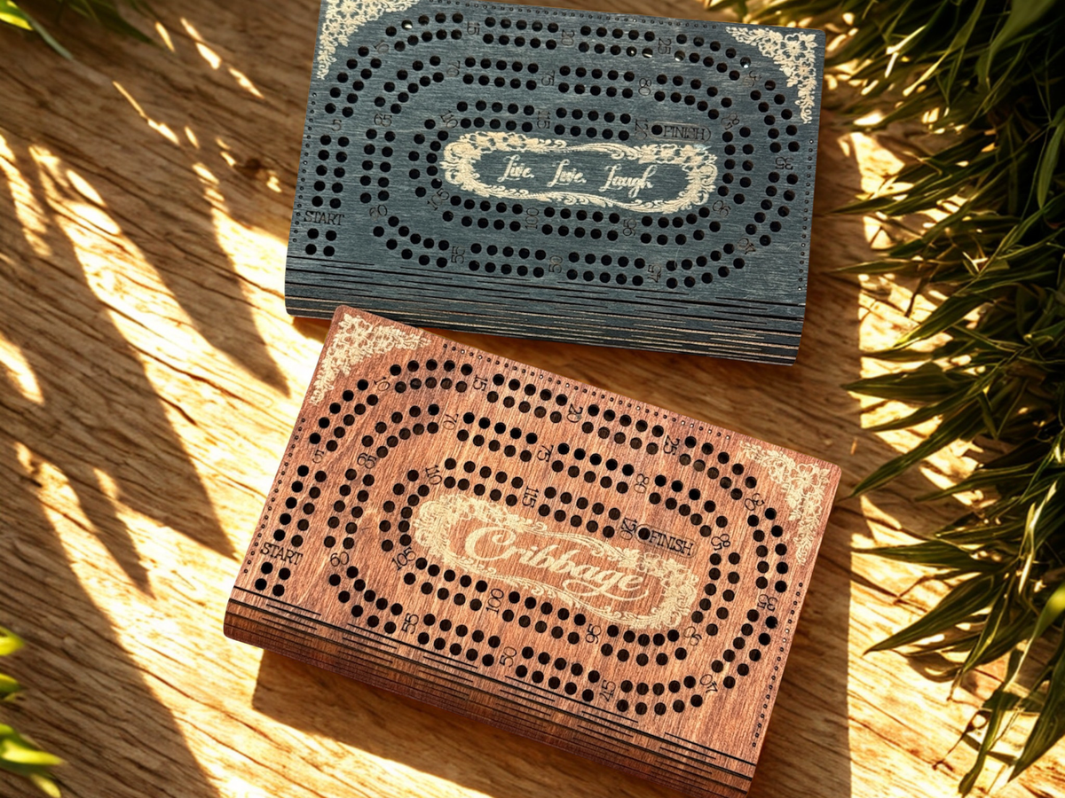 Two wooden cribbage boards on a wooden surface with plants in the background