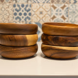 Stacks of wooden bowls on a surface with a patterned wall in the background