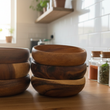 Set of wooden bowls on a kitchen counter with jars of spices in the background.