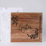 Wooden cutting board with 'Gather' and floral designs on a white background
