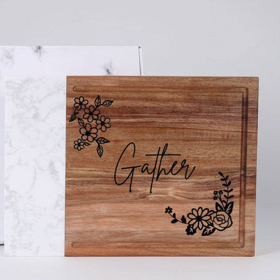 Wooden cutting board with 'Gather' and floral designs on a white background