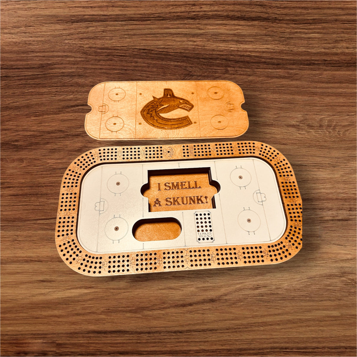 A personalized rectangular cribbage board with a hockey rink design, open to show the storage for game pieces and with a personalized engraving. A deck of cards and pegs are included.
