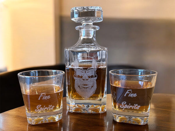 Whiskey decanter and two glasses with 'Fine Spirits' text on a wooden surface.