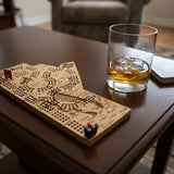 Wooden cribbage board with pegs and a glass of whiskey on a table.