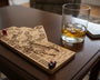Wooden cribbage board with pegs and a glass of whiskey on a table.