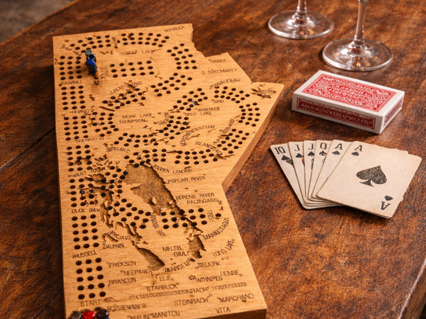 Wooden cribbage board with playing cards and wine glasses on a wooden table.