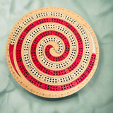 Circular wooden cribbage board with spiral design on a gray background