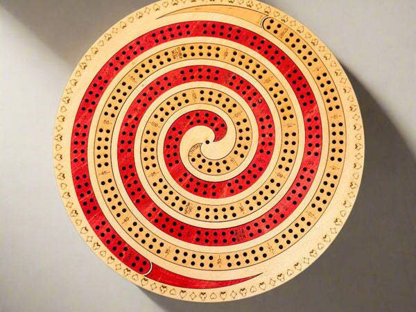 Round wooden cribbage board with red and beige spiral design on a gray background