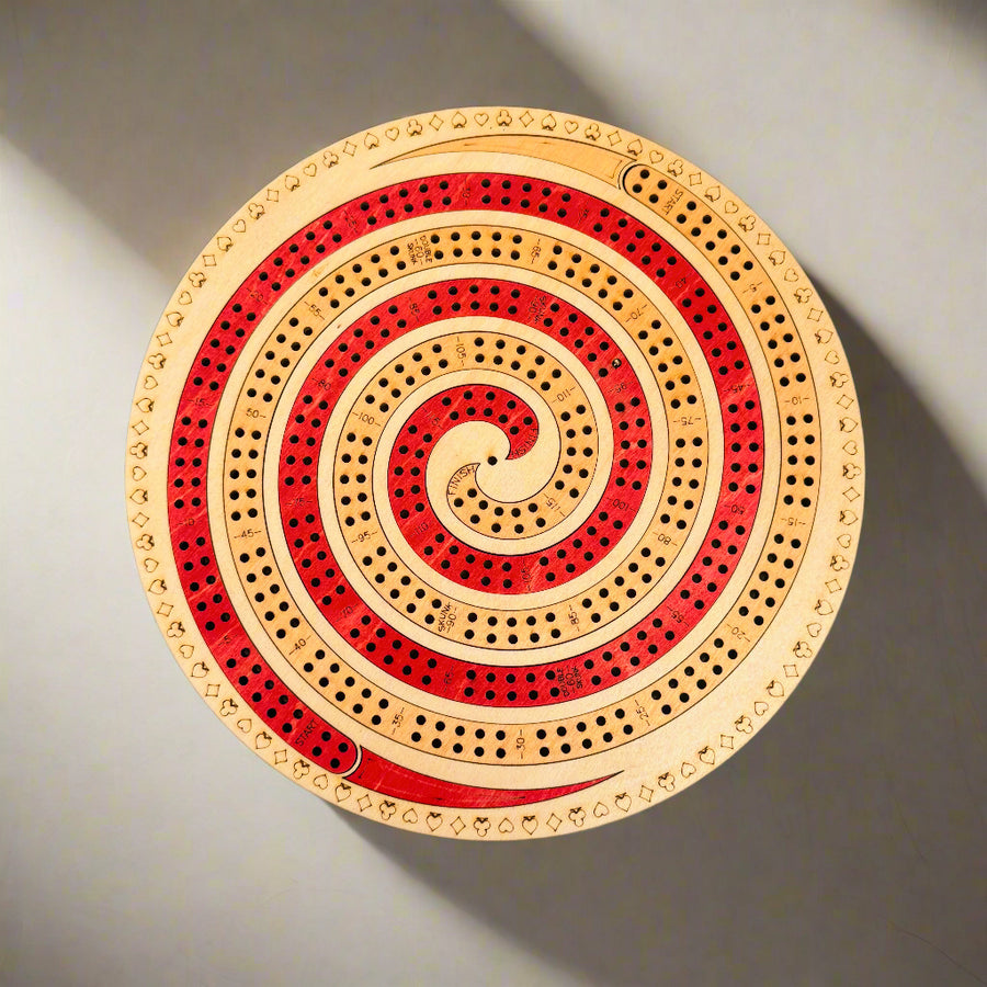 Round wooden cribbage board with red and beige spiral design on a gray background