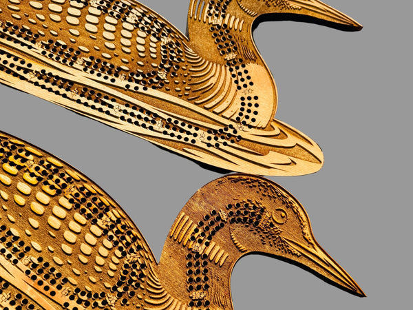 Two wooden duck-shaped cribbage boards on a wooden surface.