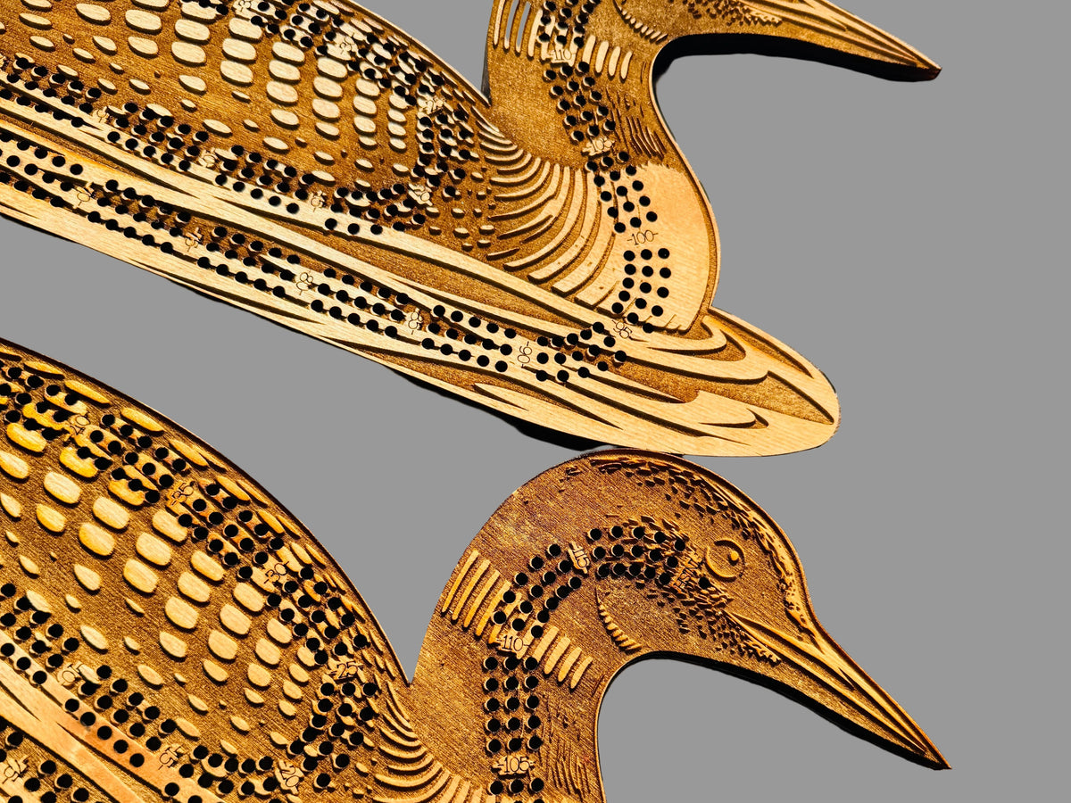 Two wooden duck-shaped cribbage boards on a wooden surface.