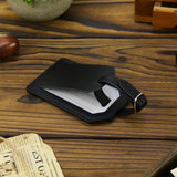 Black leather luggage tag on a wooden surface with a newspaper underneath