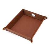 A square brown leather or faux-leather tray with a cutout handle on one side and metal snap details at the corners, shown on a plain white background.