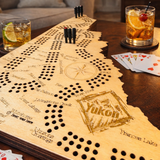 Wooden cribbage board with cards and drinks on a table