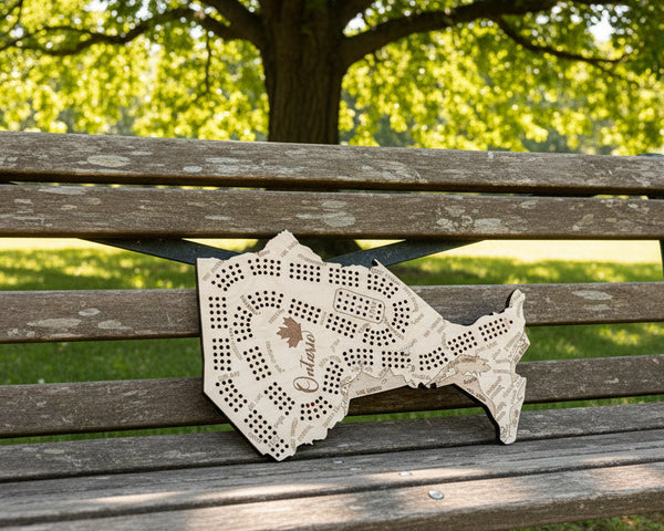 A wooden Ontario-shaped board game set displayed on a dark background, with playing cards arranged along the bottom wooden surface. The board features engraved street names, playing card suits, and the word 'Ontario' with a maple leaf.