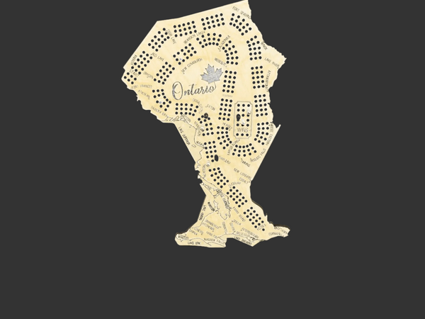 A novelty Ontario-shaped cribbage board made from a cut-out sheet of cream-colored paper, featuring printed map details, a small maple leaf, and the word 'Ontario' in script, set against a dark background.