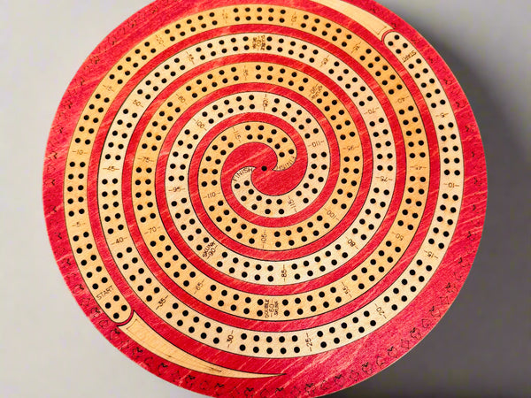 Round wooden cribbage board with red and beige spiral design on a gray background