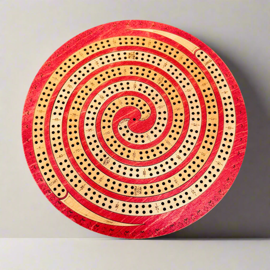 Round wooden cribbage board with red and beige spiral design on a gray background