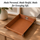 A brown leather tray with metal handles sits on a wooden table in a styled home setting, with a white banner at the top reading 'Made Personal. Made Useful.