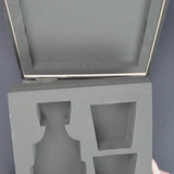 Gray foam packaging insert for a vase held by hands against a dark background