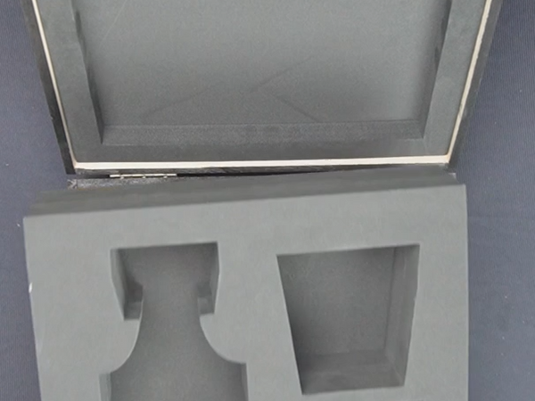 Gray foam packaging insert for a vase held by hands against a dark background
