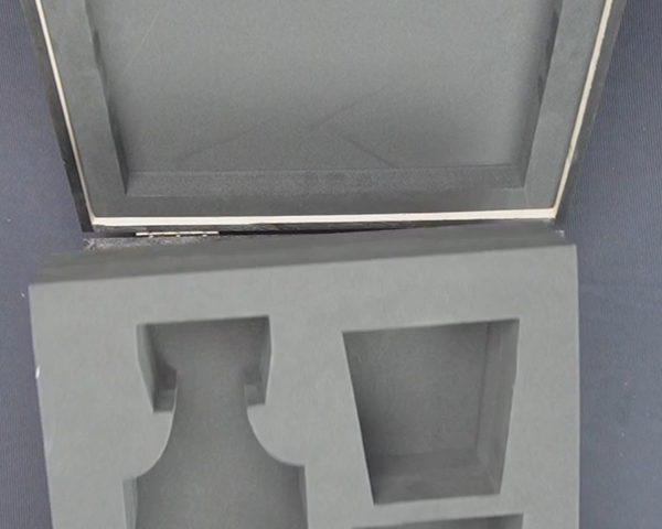 Gray foam packaging insert for a vase held by hands against a dark background