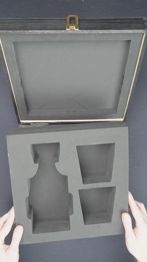 Gray foam packaging insert for a vase held by hands against a dark background